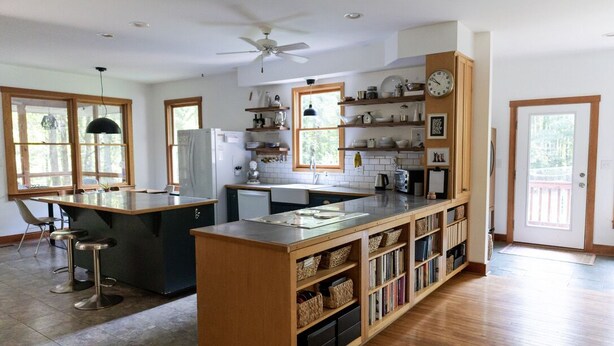 A spacious kitchen with wooden cabinetry, a central island, and a dining area with bar stools. - Cozy Athens Home on the Brook (Athens)