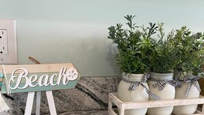 A kitchen counter with a 'Beach' sign, a potted plant arrangement, and a power outlet. - 46 by the Sea, steps to private beach & heated pool, 1-mile from Main St., ocean views,  AC, & Wi-Fi (Barnstable)