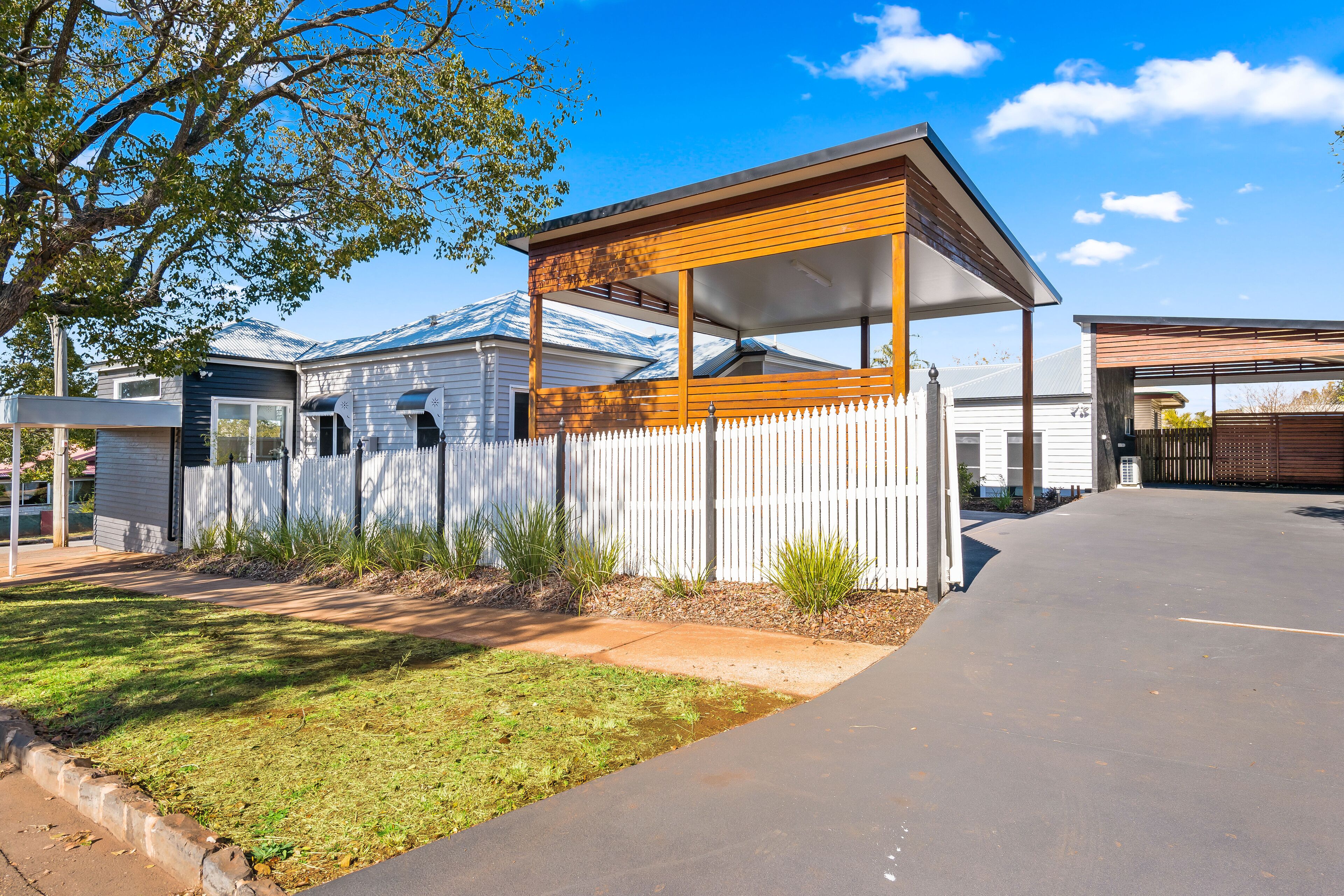 A residential property with a covered porch, a white picket fence, and a paved driveway.