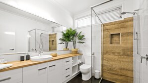 Ett modernt badrum med en duschavdelning med glasväggar, en vägg med träpanel, en stor spegel och en krukväxt.
