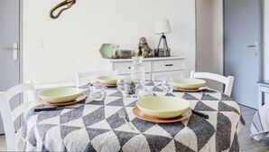 A dining area with a checkered tablecloth, white chairs, and a wall-mounted decorative piece. - Les Villageoises by Interhome (Le Barcarès)