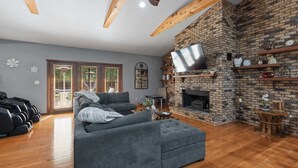 A living room with a brick fireplace, a large grey sofa, and a TV mounted on the wall.