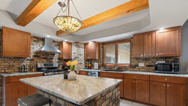 A kitchen with a central island, wooden cabinets, a stone accent wall, and a hanging light fixture.