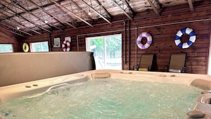 A hot tub with a wooden interior, a window with a view of greenery, and life rings on the wall.