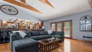 A spacious living room with a large sectional sofa, a wooden coffee table, and a kitchen in the background.