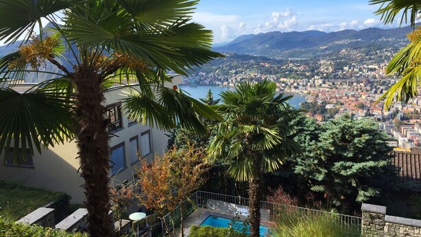 Zona residencial con piscina, palmeras y vistas a un paisaje urbano con montañas al fondo.