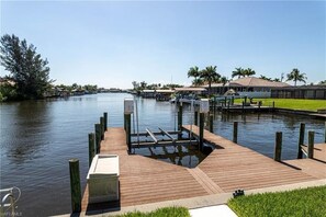 A wooden dock extending into calm water with a grassy area in the foreground.