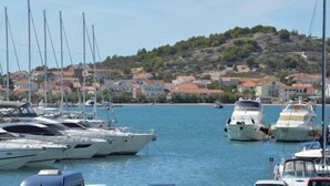 Un puerto deportivo con varios yates amarrados, un paisaje montañoso de fondo y edificios con tejados rojos.
