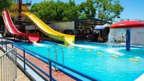 Una piscina con dos toboganes, una fuente y una zona de estar techada.