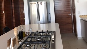 A modern kitchen with a central island, stainless steel appliances, and a wooden accent wall. - Beautiful Golf Course Views - Relax! (Nuevo Vallarta)