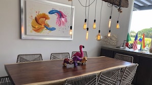 A dining area with a wooden table and wicker chairs, a colorful painting, and a hanging light fixture. - Beautiful Golf Course Views - Relax! (Nuevo Vallarta)