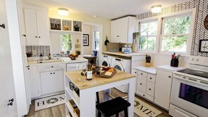 Cocina compacta con armarios blancos, encimera de madera, fregadero, lavadora y estufa.