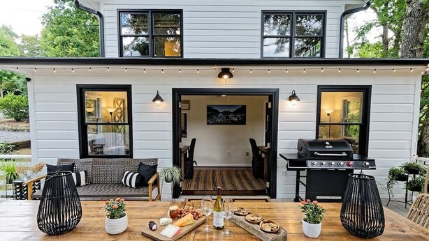 Una casa moderna de dos pisos con terraza, asientos al aire libre, una parrilla y una mesa de comedor con comida y bebidas.
