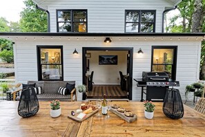 Ein modernes, zweistöckiges Haus mit Terrasse, Sitzgelegenheit im Freien, Grill und einem Esstisch, gedeckt mit Speisen und Getränken.