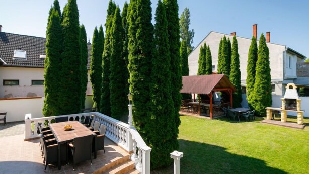 A patio with a dining table and chairs, surrounded by tall cypress trees. - Big Thuja by Interhome (Balatonföldvár)