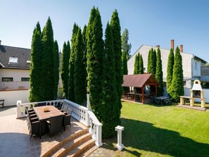 Eine Terrasse mit Esstisch und Stühlen, umgeben von hohen Zypressen.