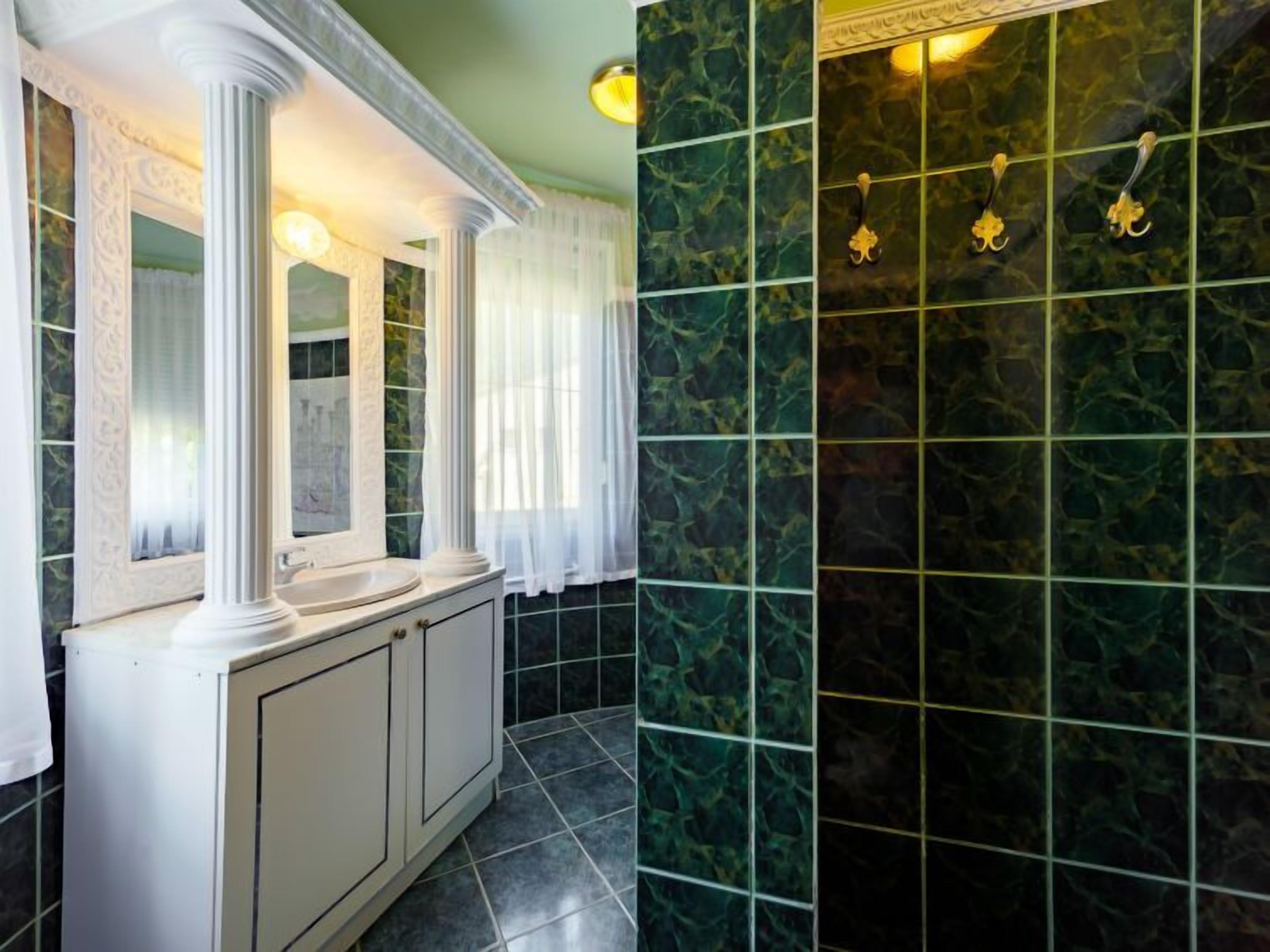 Un bagno con un vanità bianca, uno specchio e uno schienale in marmo verde.
