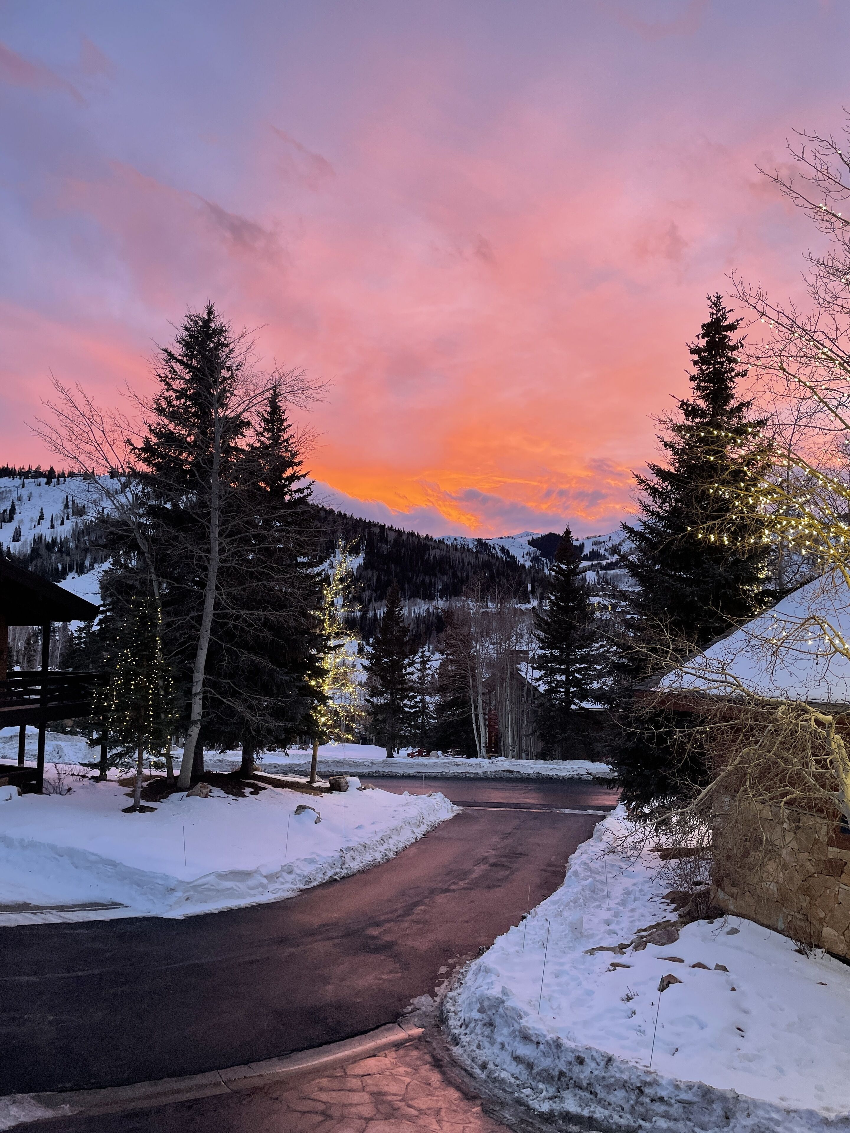 Uma estrada coberta de neve, com uma estrutura de madeira à esquerda e um edifício coberto de neve à direita.