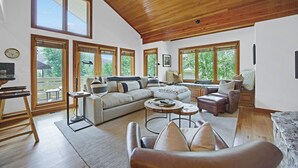 A spacious living room with a high ceiling, large windows, and a cozy seating area.