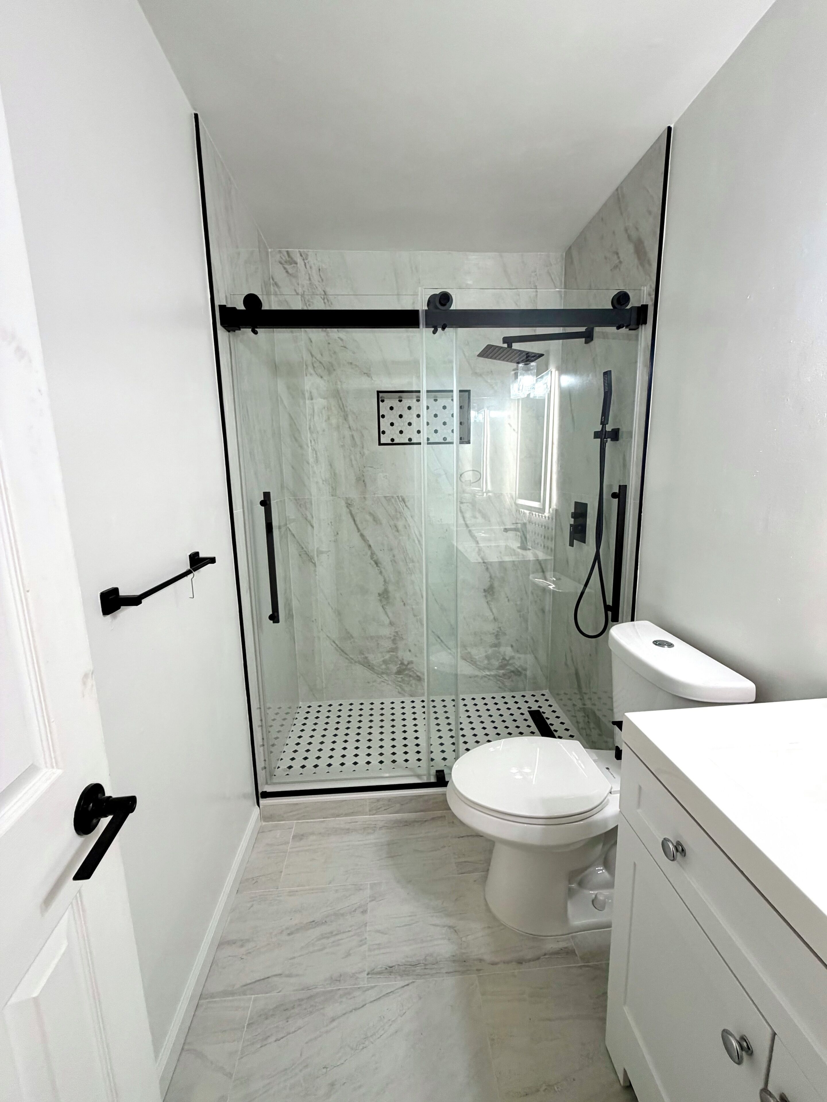 A modern bathroom with a glass-enclosed shower, a toilet, and a vanity with drawers.