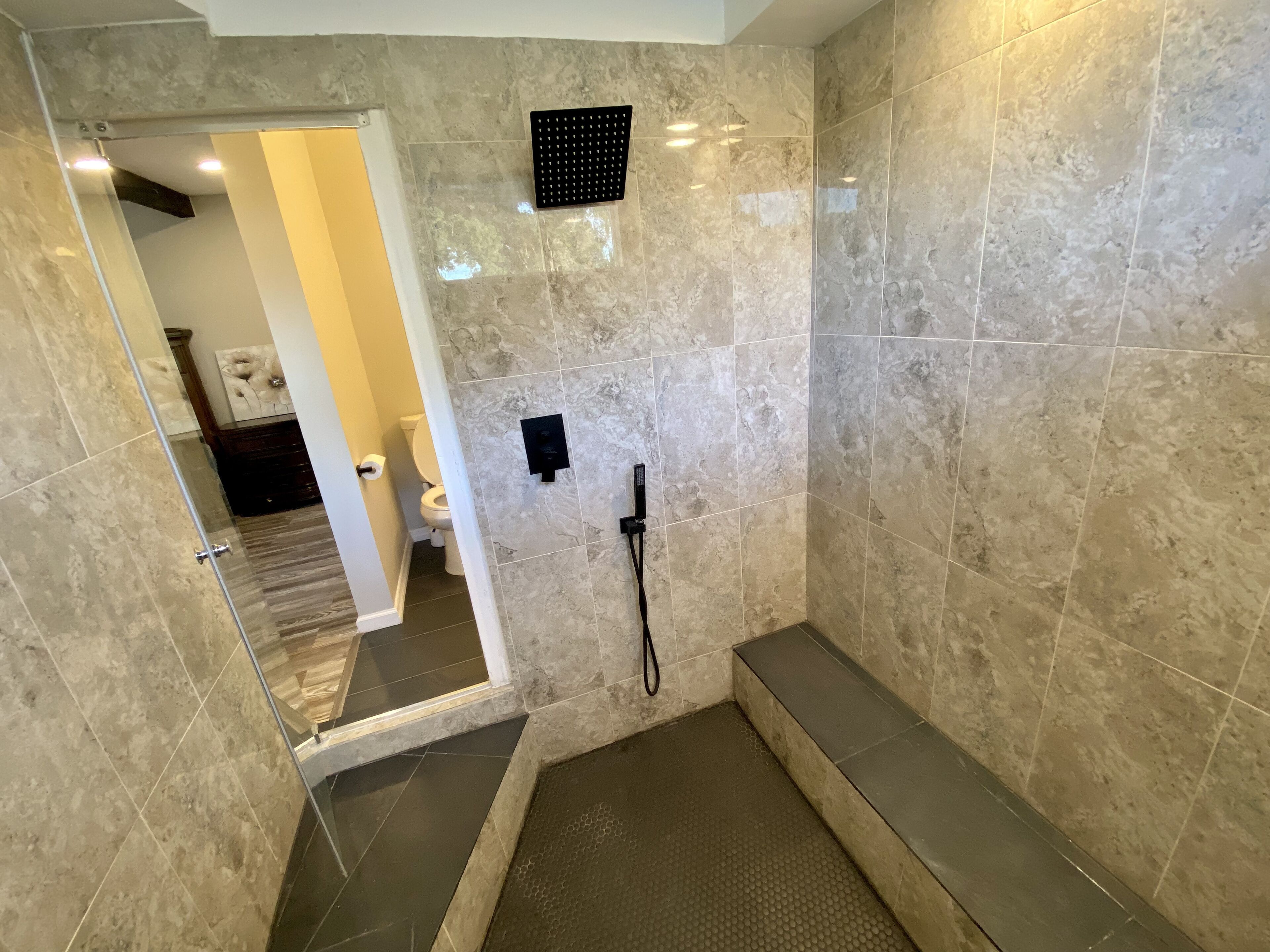 Un baño moderno con cabina de ducha, azulejos de mármol y una puerta de cristal que da a otra habitación.