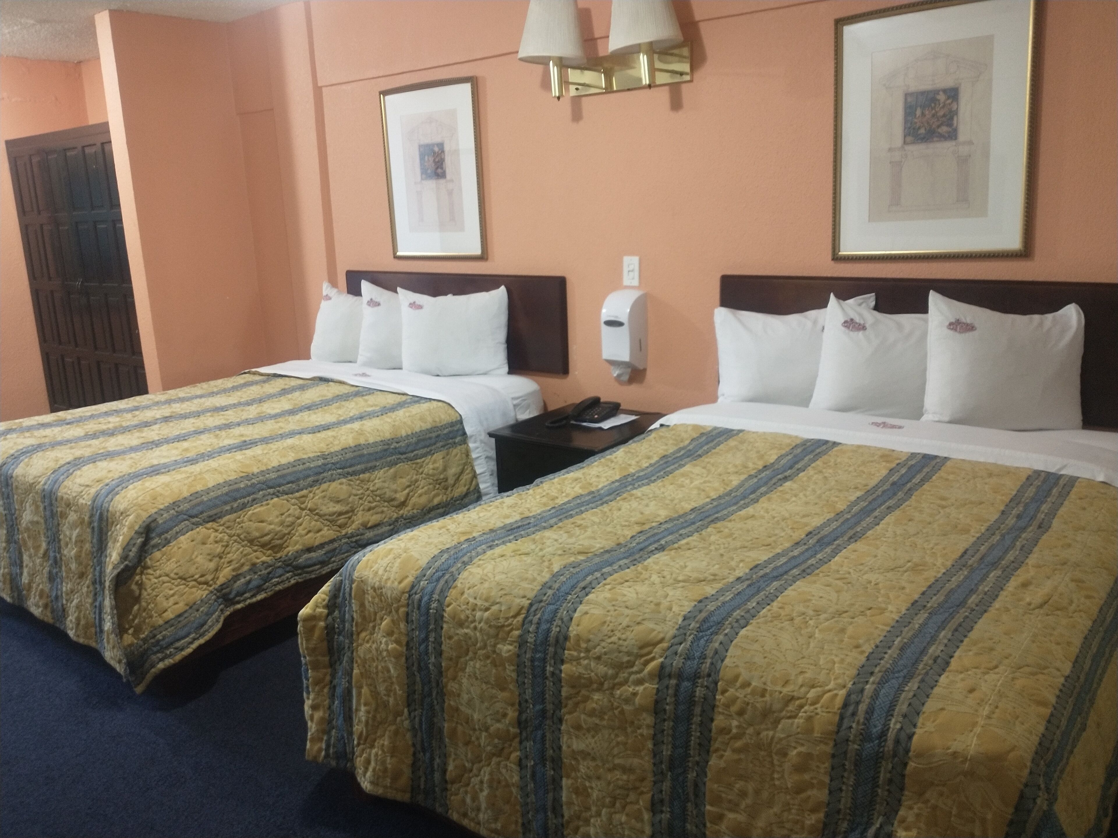Habitación de hotel con dos camas, cada una con ropa de cama a rayas, una mesita de noche, un teléfono y una lámpara fijada a la pared.