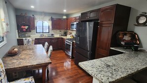 A kitchen with wooden cabinets, a stainless steel refrigerator, a microwave, and a dining area with a table and chairs.