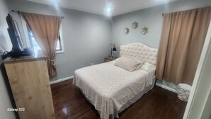A bedroom with a bed, wooden dresser, and a nightstand with a lamp.