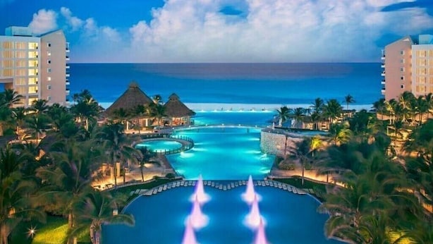 Un complexe hôtelier doté d’une grande piscine, de palmiers et offrant une vue sur l’océan.