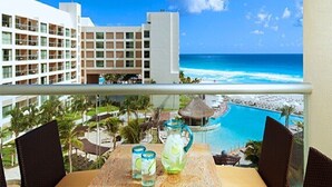 Un balcon avec une table et des chaises, donnant sur une piscine et une plage.