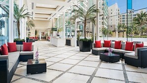Un hall d’entrée spacieux, doté d’un mobilier moderne, de grandes fenêtres et de palmiers.