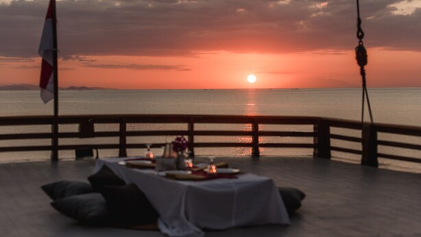 Une vue imprenable sur le coucher de soleil, depuis une terrasse où une table est dressée pour deux, avec la mer en toile de fond.