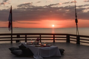A sunset view from a deck with a table set for two, overlooking the sea. - Plataran Phinisi Malayeka (Labuan Bajo)