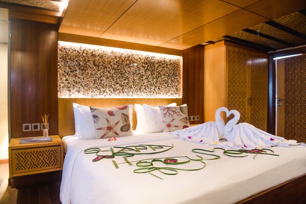 A hotel room with a neatly made bed, a decorative wall panel, and a patterned door. - Plataran Phinisi Malayeka (Labuan Bajo)