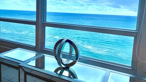 Une pièce dotée de grandes fenêtres donnant sur l’océan, une table en verre ornée d’une sculpture métallique décorative et une vue imprenable sur la mer.