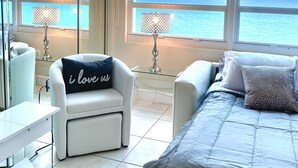 Une chambre moderne avec un lit, deux fauteuils, une petite table et de grandes fenêtres donnant sur l’océan.