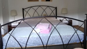 Una cama con estructura metálica, dos lámparas de noche y una pared decorada con dos cuadros.