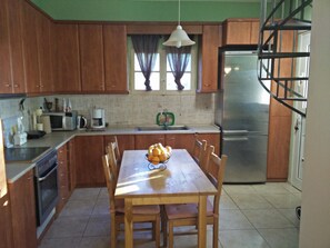 Una cocina con armarios de madera, un refrigerador de acero inoxidable, una mesa de comedor con sillas y una lámpara colgante.