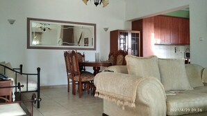 Una sala de estar con un sofá, una mesa de comedor con sillas, un espejo y una zona de cocina con armarios.
