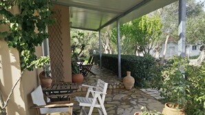 Un patio exterior con suelo de piedra, mobiliario de madera y plantas en macetas.