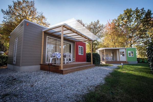 A small, two-story mobile home with a covered porch and a gravel driveway.