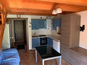 Cozinha compacta com armários azuis, bancada preta e teto de madeira.