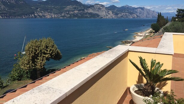 A balcony with a view of a lake, mountains, and a clear sky.
