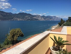 A balcony with a view of a lake, mountains, and a clear sky. - Modern Apartment With Large Terrace Malcesine (Brenzone sul Garda)