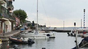 A marina with various boats docked, a pier extending into the water, and buildings with balconies on the left.
