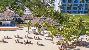 A beach resort with thatched-roof structures, palm trees, and sun loungers. - Cana Rock Pool View Punta Cana (Punta Cana)