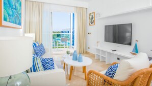 A modern living room with a TV, white furniture, a balcony with a pool, and a view of a building. - Cana Rock Pool View Punta Cana (Punta Cana)