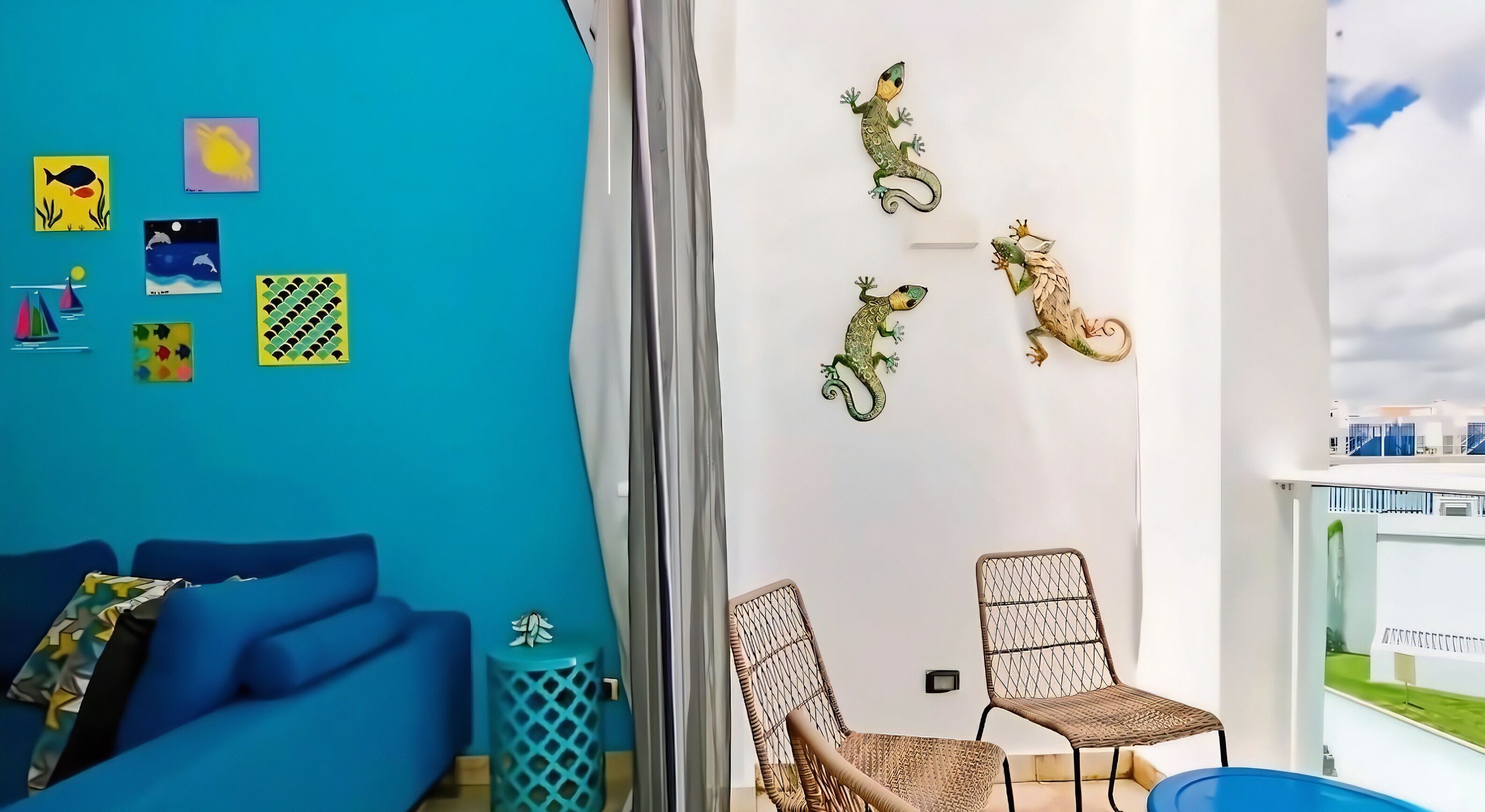 Una habitación con un sofá azul, dos sillones de mimbre, una pared blanca con detalles decorativos y un balcón con barandilla.