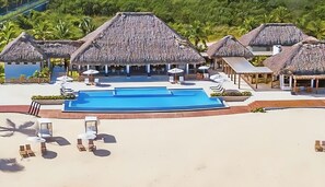 Un resort con piscina centrale, edifici a tetto di paglia e lettini prendisole.
