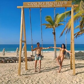 A beach club sign with 'CANA BAY BEACH CLUB LIVE LAUGH LOVE' and a swing set with two people. - Penthouse 335 Cana Rock 🎸 De Lux En Punta Cana (Punta Cana)